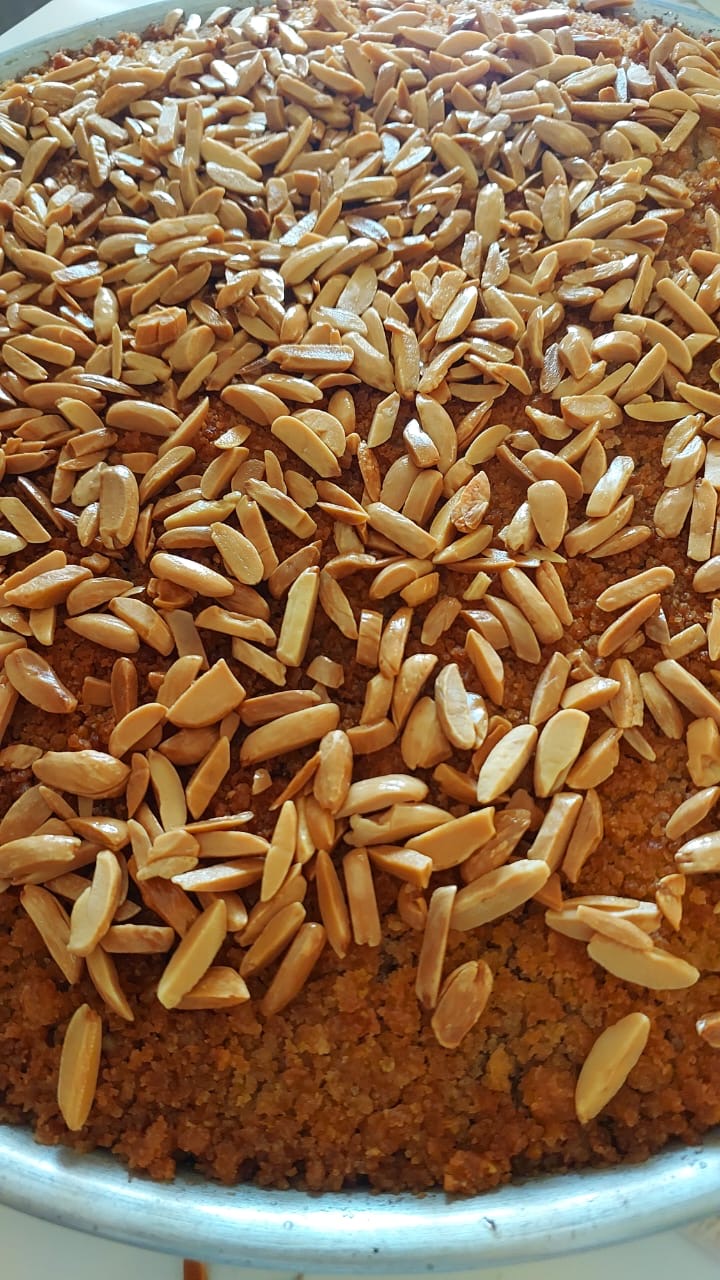 A close-up view of roasted peanuts or almonds scattered across a brown textured surface inside a metal bowl or tray.