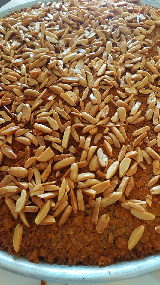 A close-up view of roasted peanuts or almonds scattered across a brown textured surface inside a metal bowl or tray.